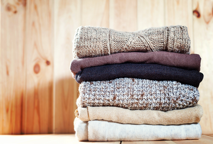 Knit cozy sweater folded in a pile on wooden background .Warm the concept