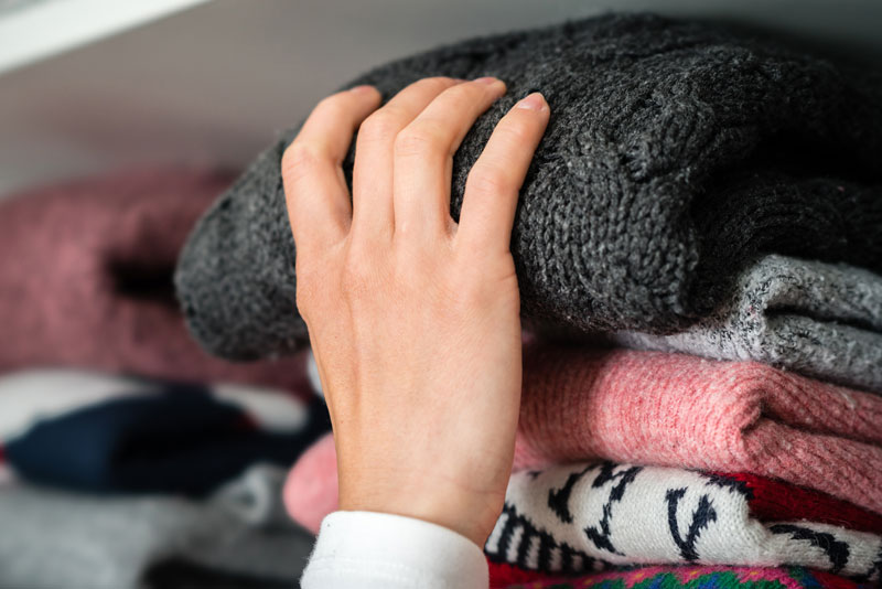 grabbing sweaters from a closet shelf