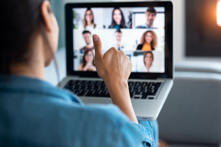 Business woman making video call and showing thumb up to laptop on the online briefing while sit on sofa at home. GettyImages 1249627169